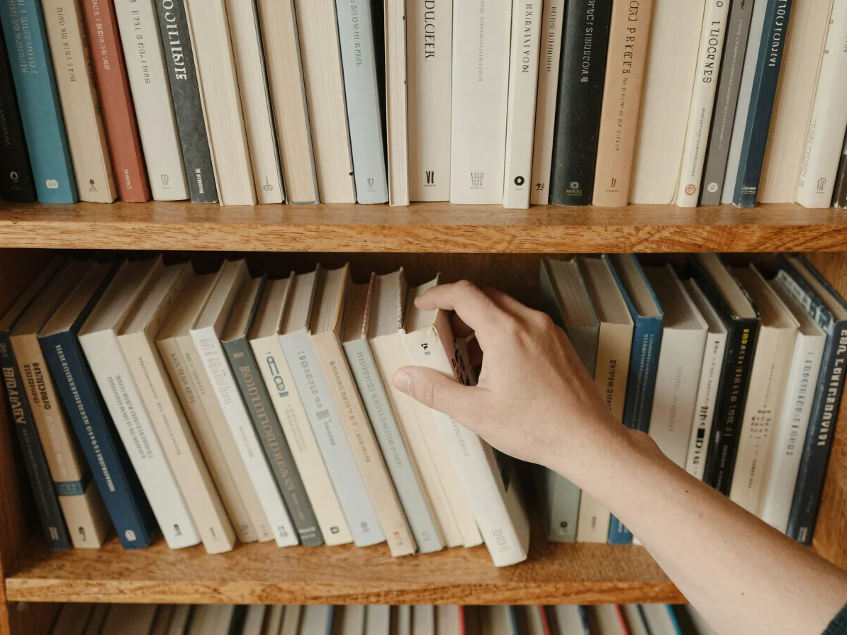 Overhead view of a hand selecting a book from a neat row of volum